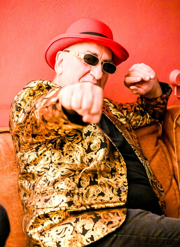 Bassist Nello met rode hoed en gouden vest, vuist naar de camera